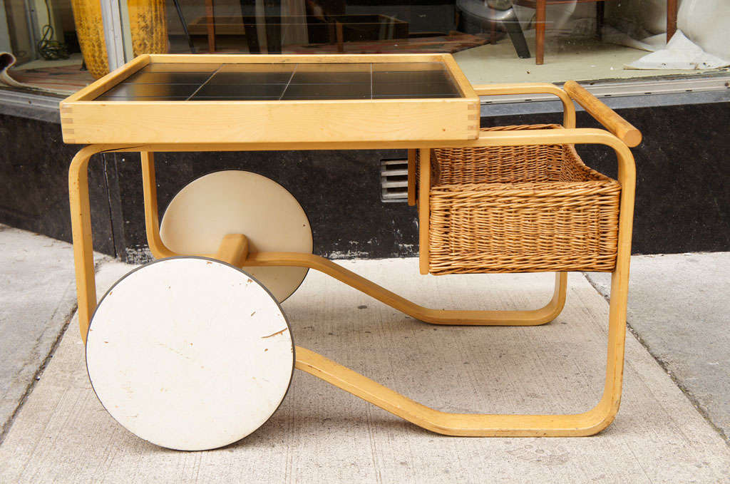 A bar cart designed by Alvar Aalto for Artek in ash with black tile top and basket weave tray.   