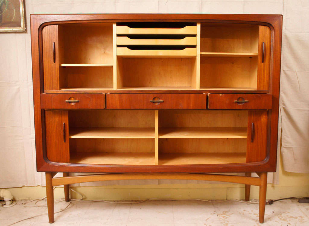1950's credenza in teakwood with tambour doors, interior compartments with trays for cutlery, three central drawers with brass handles and cupboards below.    Danish mid-century modern