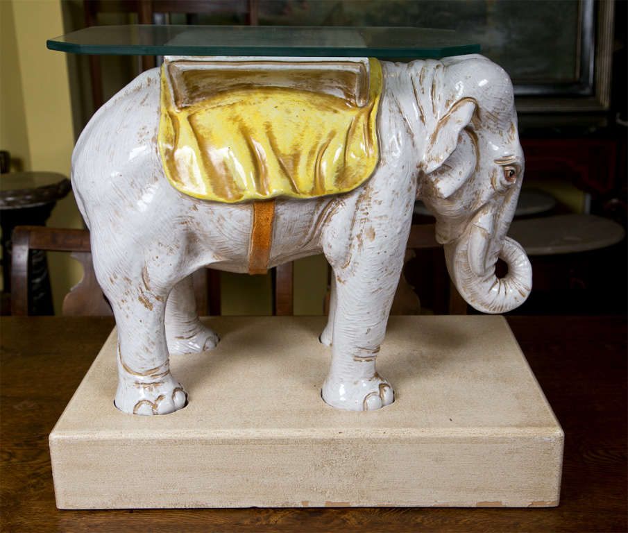 Pair of ceramic elephant side tables with glass tops, raised on block bases.