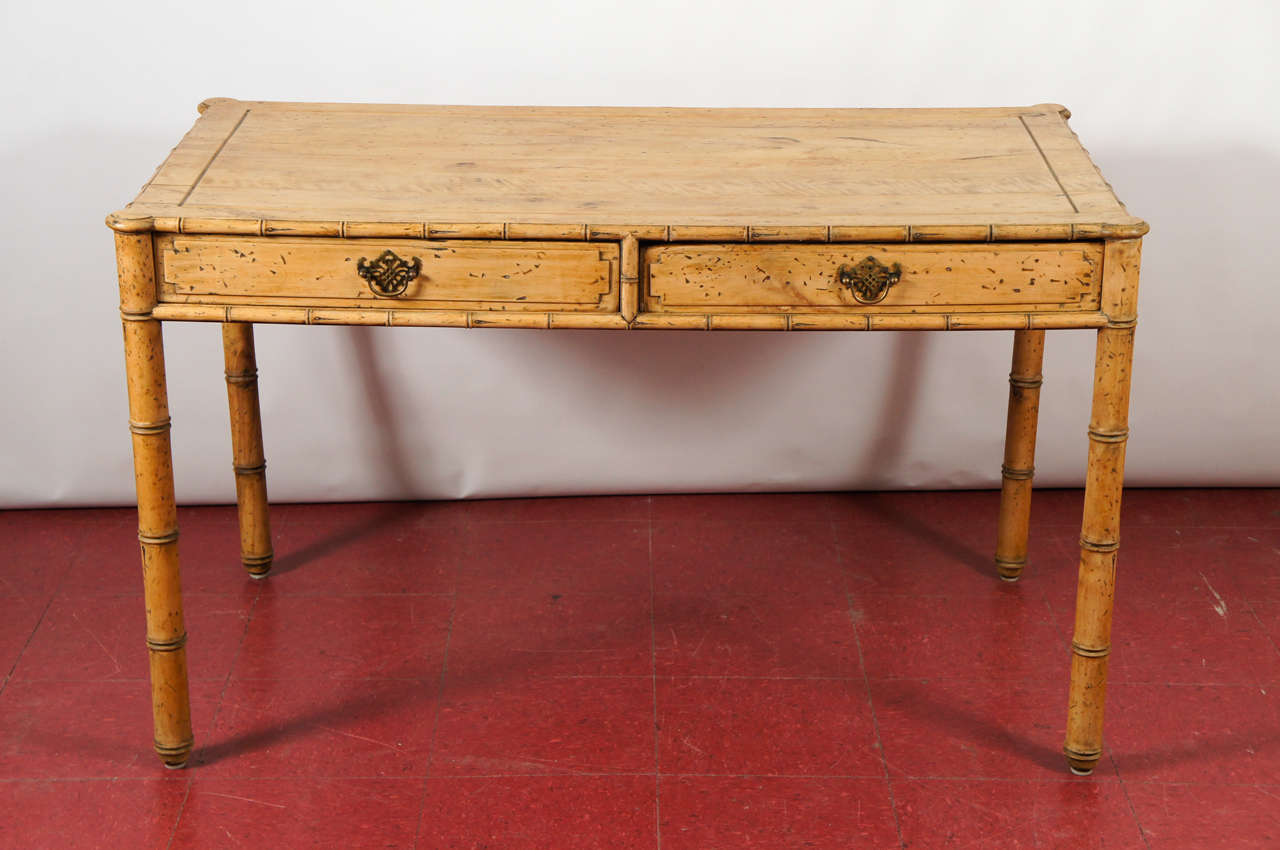 Faux bamboo desk has two paneled drawers with brass filigree handles and paneled side and back aprons.  The desk is made of natural grained and spotted wood. The label reads 