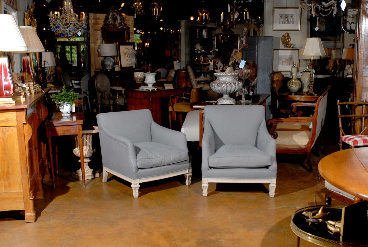 A pair of French 19th century “His & Hers” club chairs with blue grey upholstery. Each of this pair of French club chairs from the 19th century features a fully upholstered frame with low seat raised on two short tapered feet in the front. Adorned