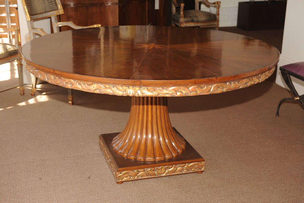 Beautiful hand-carved walnut dining table, the bookmatched veneer top of pie shaped pieces culminating in a fruitwood star, the apron and base elaborately carved with vines and branches which are finished in gold leaf above a fluted splayed pedestal