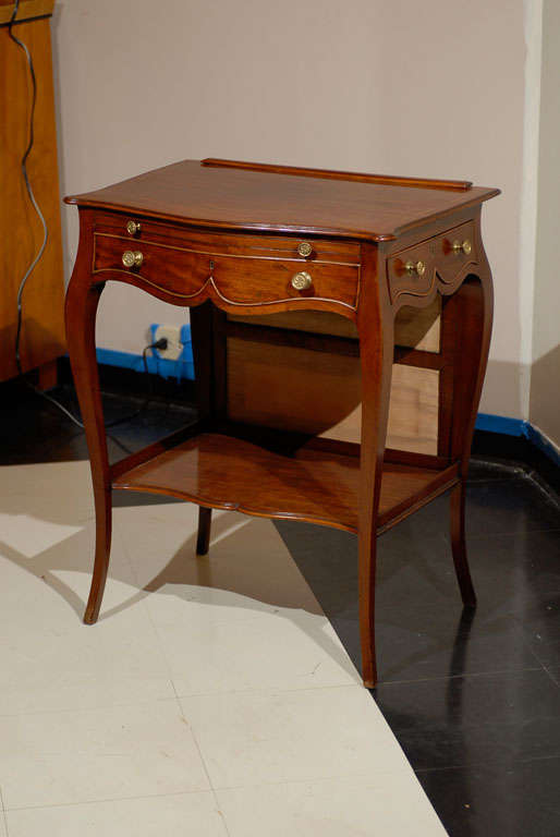 George III circa 1800-1820 mahogany lady's writing table. Made in Britian in the French style. The front is serpentine in shape with a pull-out work surface that slides over a false front drawer. The right side has one deep, fitted drawer that