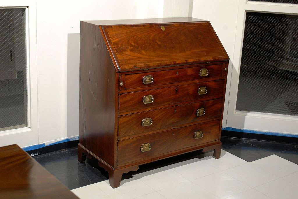 Mahogany George III (circa 1800-1820) slant top, drop front desk.  Mahogany top with ebony and satin wood stringing, mahogany banding, and chamfered edge. Graduated drawers with brass pulls. Bracket feet.  Top opens revealing writing surface, slots,
