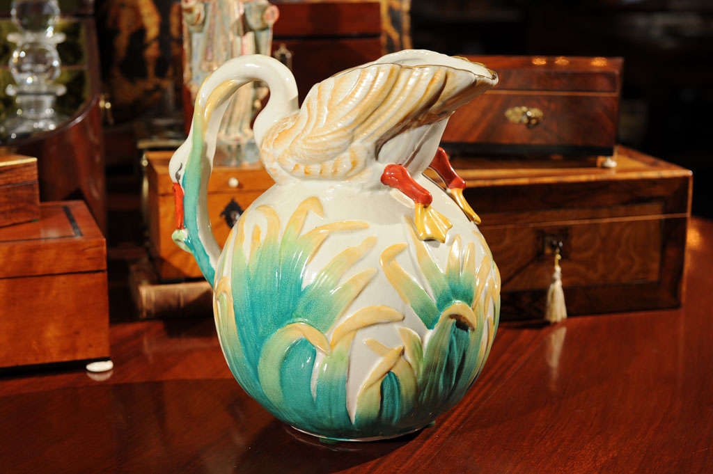 The large globe form surrounded by a relief of golden yellow and teal green tipped tall grass surmounted by a swan, it's neck downswept with tomato red beak to complete the handle.  Gilted spout trim.