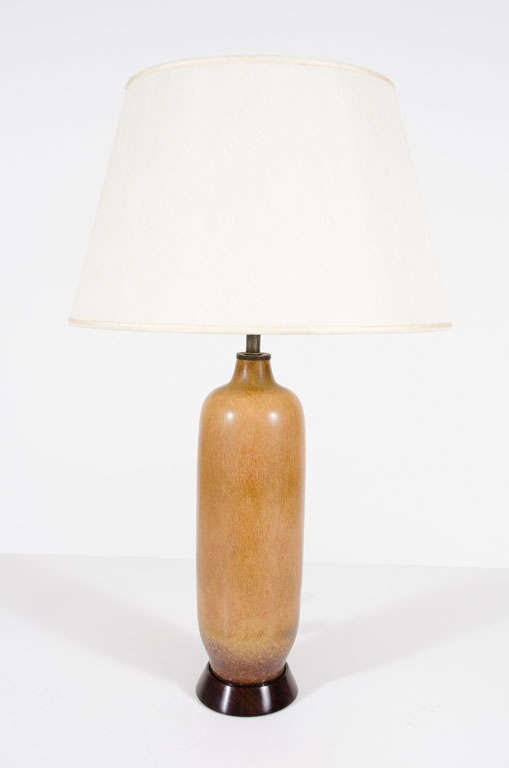 A beautiful table lamp with an elongated bullet form body, slender neck and tapered bottom in a hares fur glaze resting on a circular wooden base. By Gunnar Nyland for Rorstrand. Sweden, circa 1950.