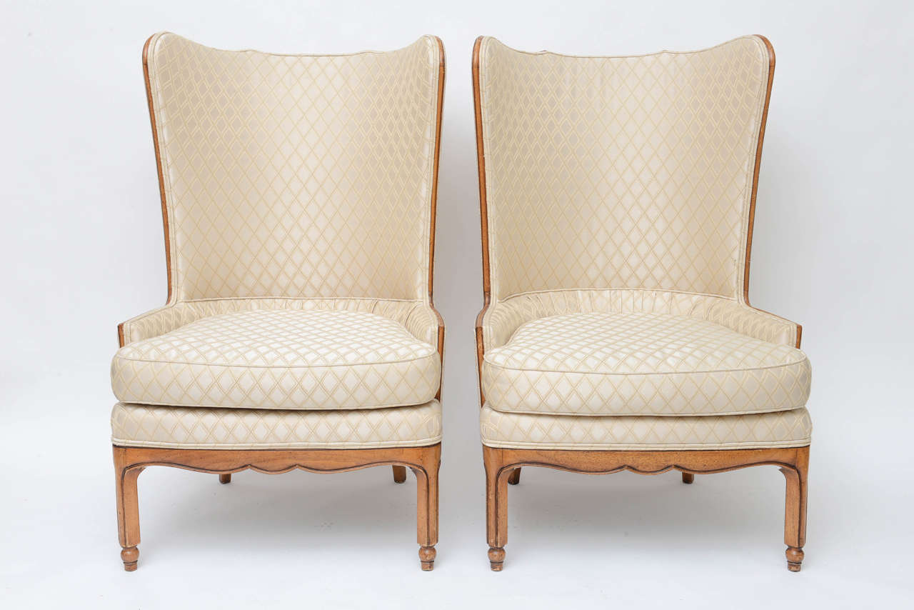 Pair of high back wing tip club chairs, in the manner of Grosfeld house. Original upholstery, crème silk viscose textile with cross-hatched embroidered diamond-shape pattern throughout. Walnut frame, with down-filled seat cushion, tight back seat