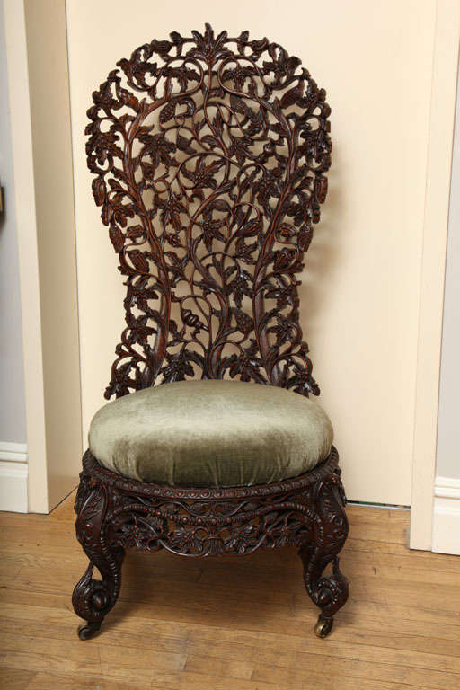 A hand carved rosewood Burmese slipper chair with shaped high back, the open fret back with leaves, vines and flowers. The front cabriole legs and splayed back legs terminating in castors, the slip seat upholstered in velvet.