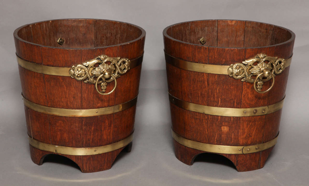 Fine and unusual pair of William IV oak and gilt brass mounted wine buckets, having staved construction, brass outer and iron inner banding, retaining original foliate and bead decorated gilt brass handles, the bases relieved with arched feet, both