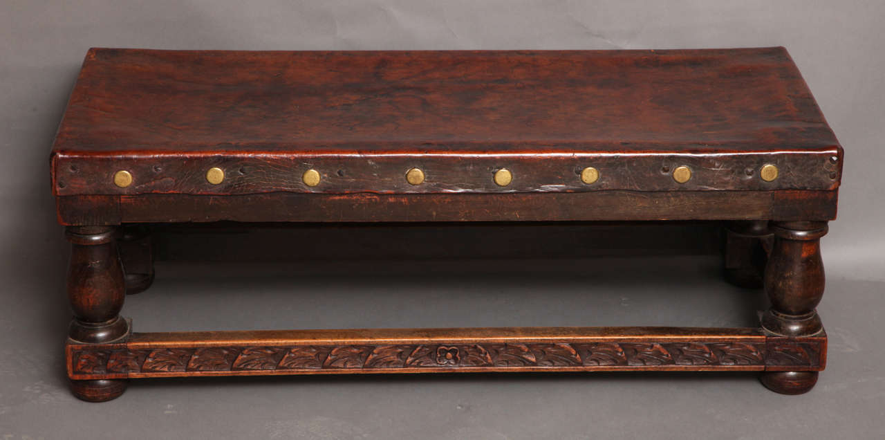 English early 20th Century Arts and Crafts period studded leather top coffee table, the richly patinated full hide top with brass stud decoration, on balustrade turned legs joined by foliate carved stretchers.