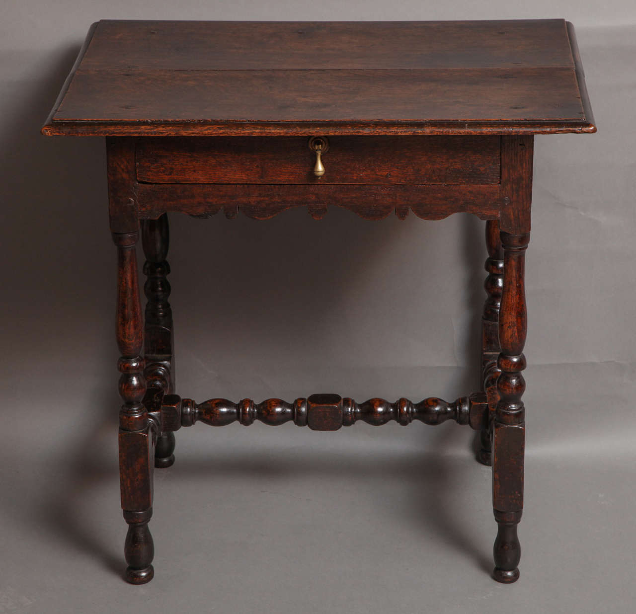 Lovely early 18th century oak side table, the richly patinated two board top having thumb molded edge, over single drawer, over richly scalloped apron, over boldly turned legs joined by turned 
