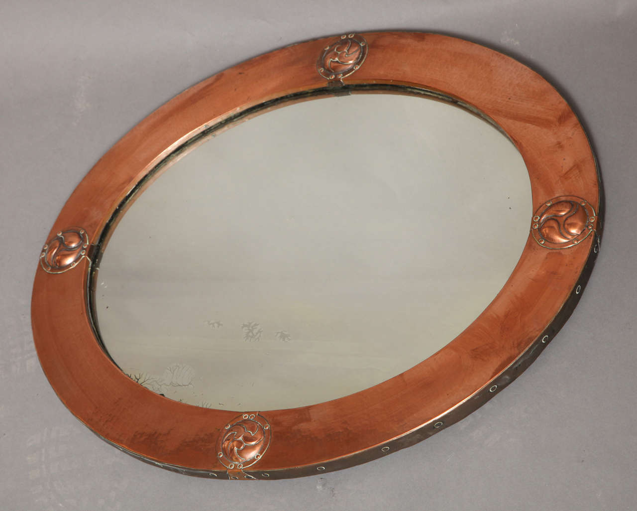 Fine English Arts and Crafts period hammered copper oval mirror by Liberty of London, the bezel frame decorated with hammered copper cabochons depicting Celtic swirls, the whole with mellow closing surface and good design.  The back retains original