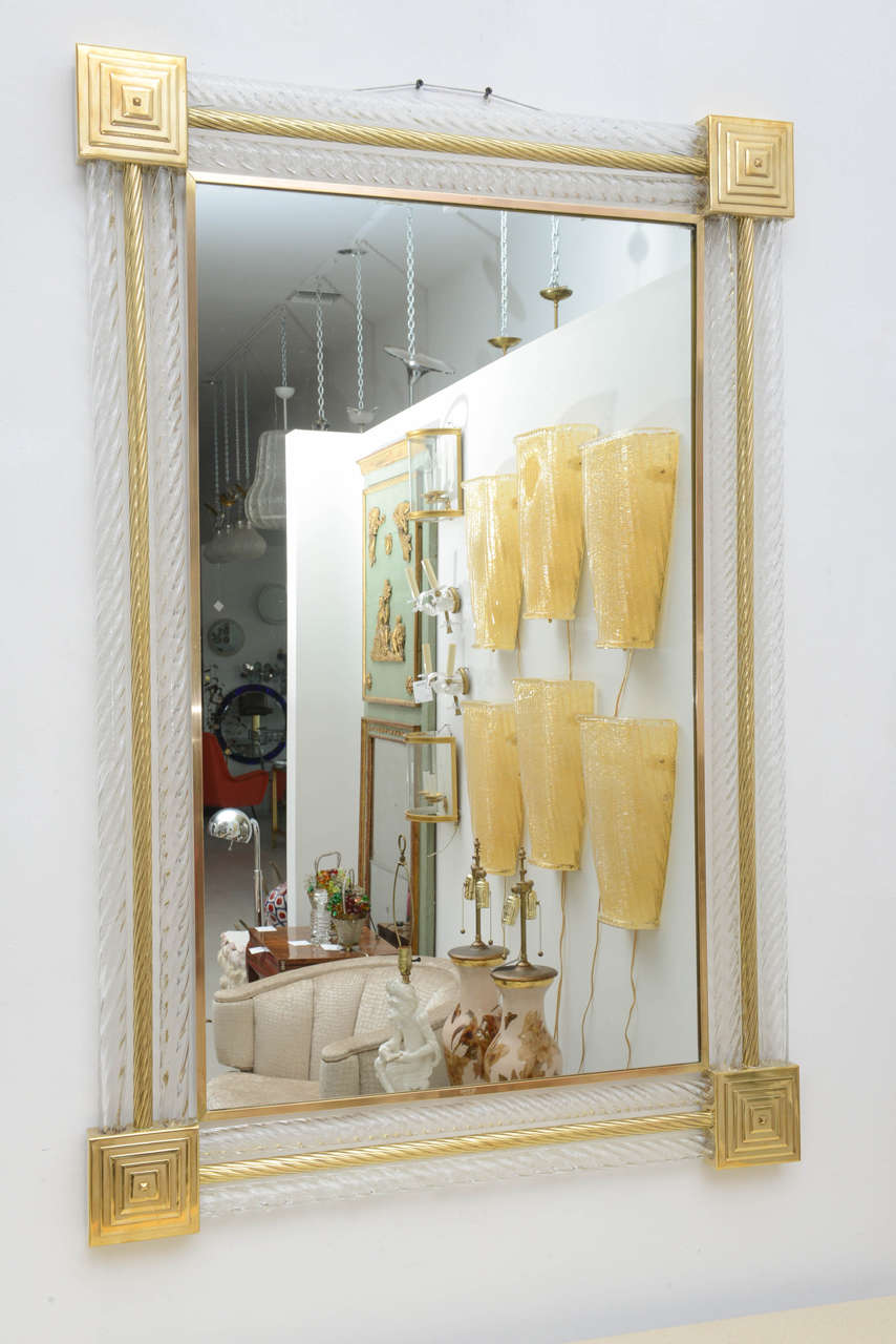 Two matching Murano glass mirrors with square brass pyramids in the corners and twisted brass rods with alternating twisted clear Murano glass rods. The frame of each mirror has a satin finish flat frame of brass, stamped in the center base with