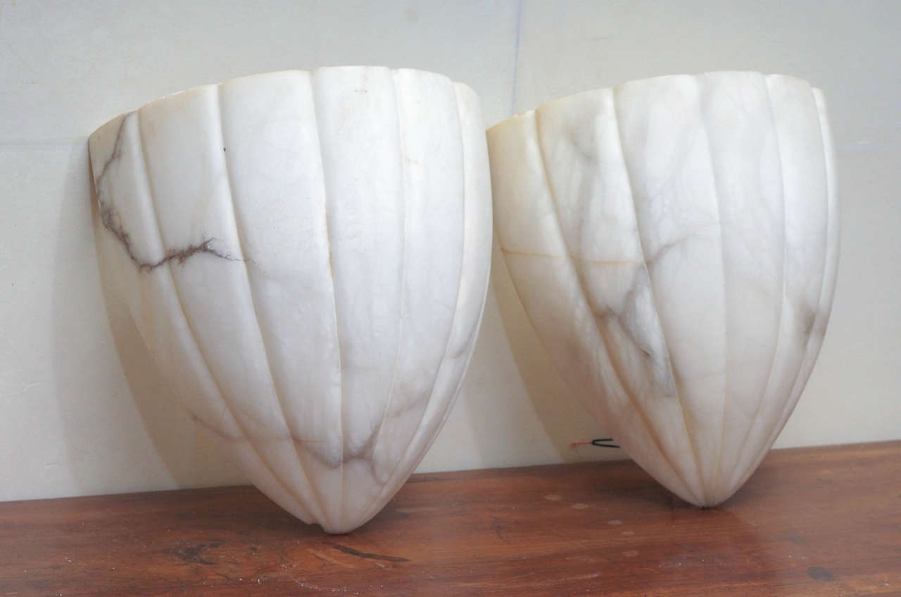 These are a pair of unusually shaped great scale alabaster sconces. When lighted, the alabaster gives off a warm, translucent glow.