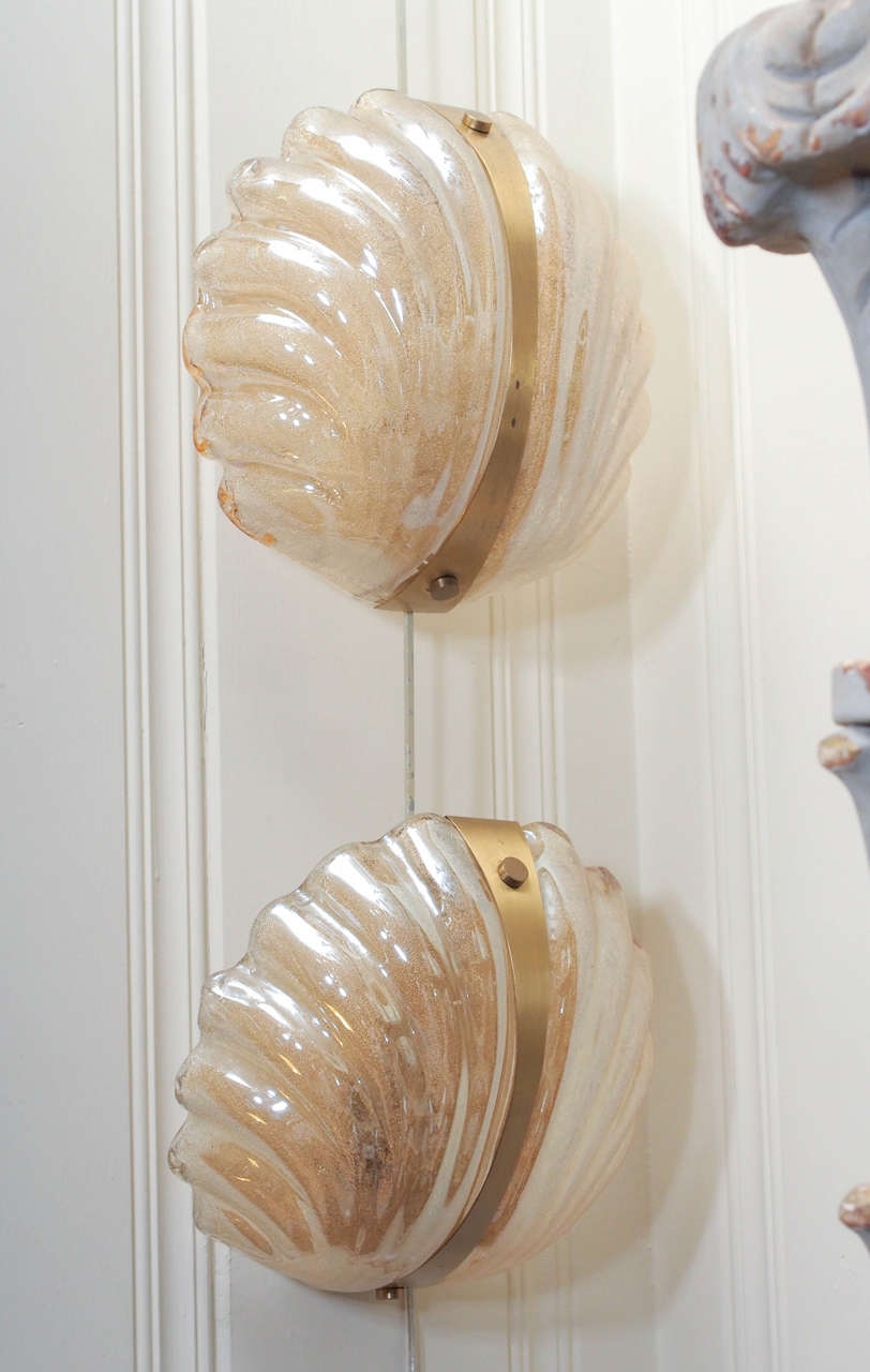 The scalloped shell shaped Murano glass sconces have an iridescent pearl glaze with gold leaf fused into glass. They are set off by brass mounts and provide a golden glow when lighted, Italian.