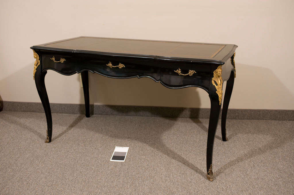 This is a beautiful vintage (1950s) French Louis XV writing desk done in a sleek black lacquer finish and features solid brass ormolu and three spacious pull-out drawers. The top is adorned with smooth leather and boasts gorgeous gold-tooling around