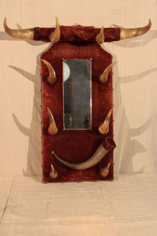 Exquisite American Folk Art Hat Rack with worn red velvet backboard and applied mirror;  at top, a lateral-mounted crossbar with four horns presides over three pairs of vertically-oriented horns in graduated sizes flanking the small vertical mirror