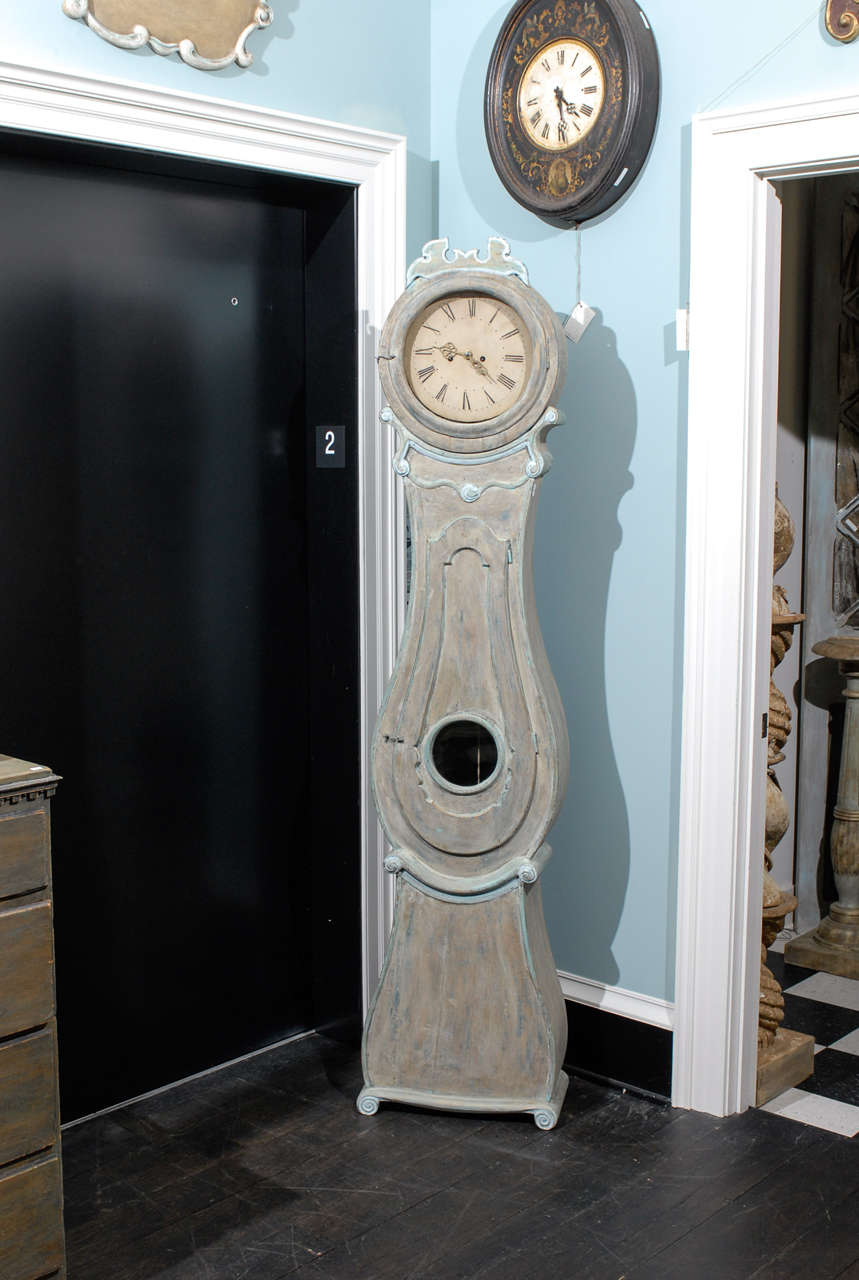 This is a 19th century Swedish tall clock, which is sometimes referred to as a Mora Clock.
 
This clock is an understated grey with subtle blue highlights.  The crown and neck are trimmed with stunning bluish white that seems to jump from the