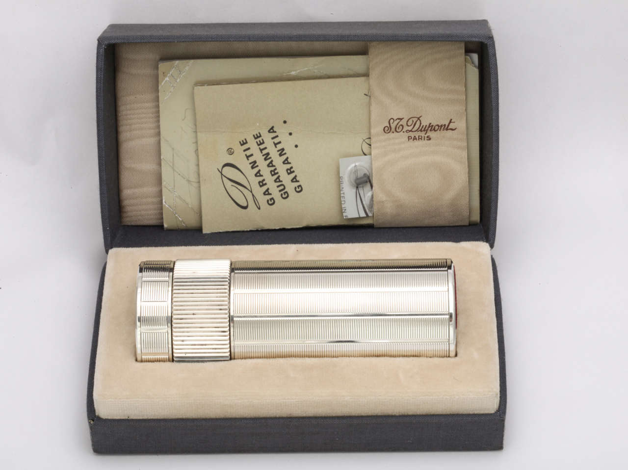 A nice silver plated table lighter by S.T. Dupont in the original fitted box. The engine turned detailing in a columnar design is quite striking and it contrasts nicely with the ridged wheel which rotates to light the flame. This lighter was