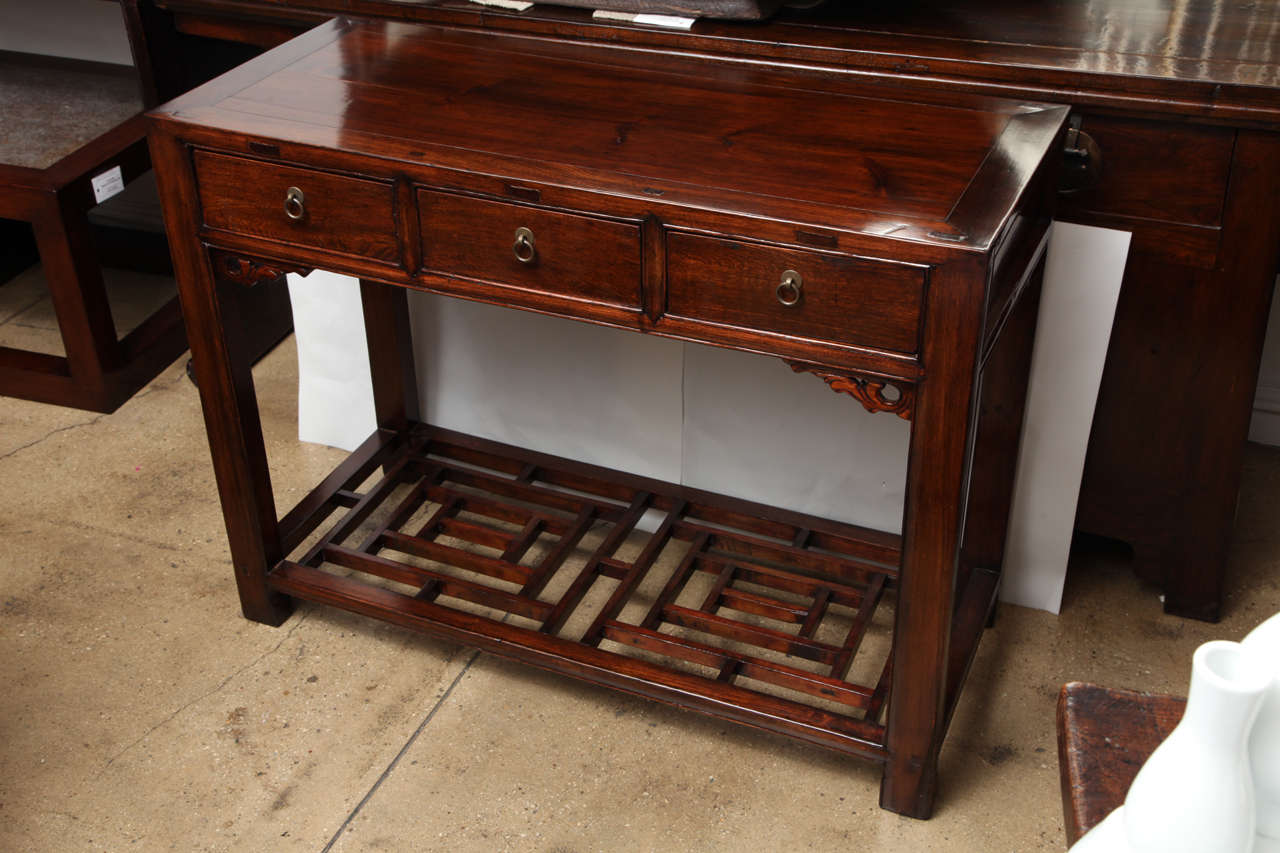 A three-drawer elmwood table or desk with a low lattice shelf.