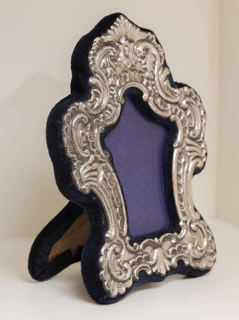 This is a charming repoussé Stand-up frame. It is small with the traditional blue velvet lining. It has wonderfully engraved scrolls and elaborately detailed and reticulated designs in sterling silver. The sterling silver has a shiny, glazed