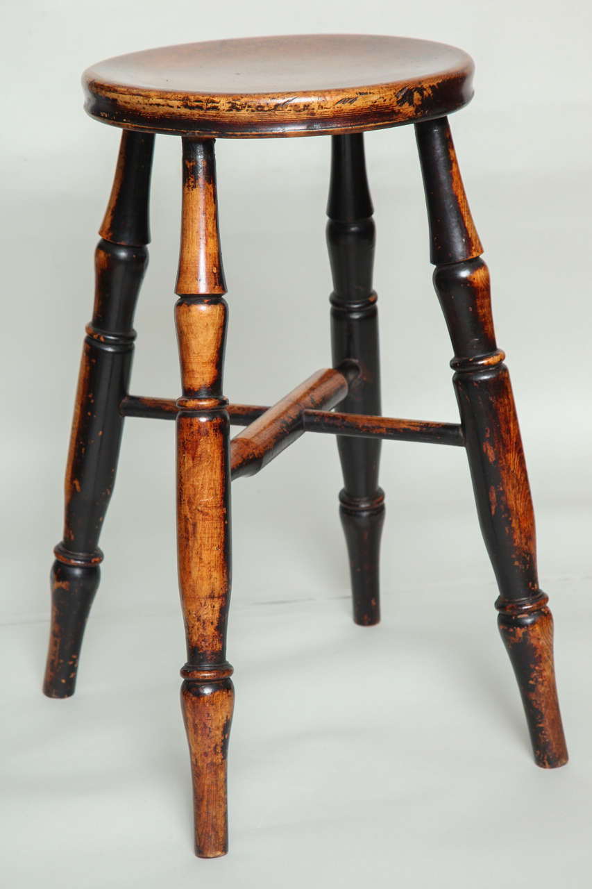 An English country stool with round dished top over four turned legs joined by cross stretcher, having the most wonderful surface showing wear and contrasting light and dark color.