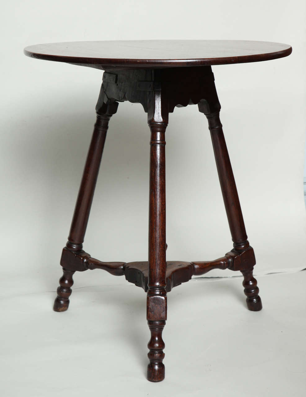 Unusual 18th century Welsh oak cricket table, the circular top with bullnose edge, over cupid bow scalloped apron, the three balustrade turned splayed legs joined by turned three spoke stretcher base having a turned central finial, several old iron