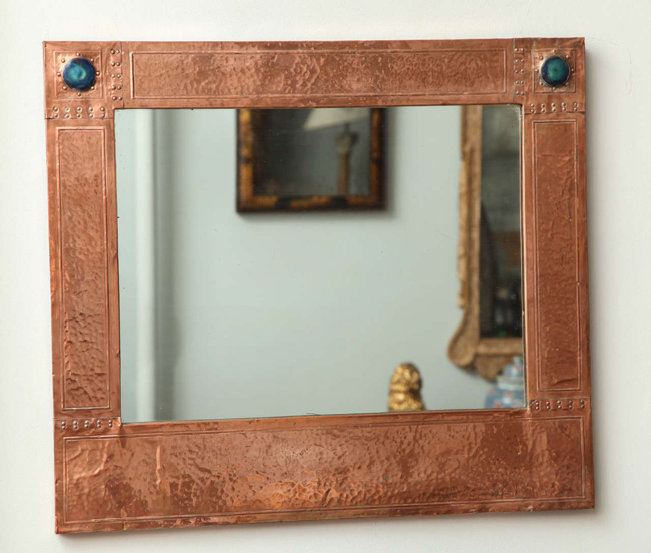 Good English Arts and Crafts hammered copper mirror probably by Liberty and Co, circa 1890, having hand hammered paneled sides with double row of riveted seams, the two upper corners with enamel 