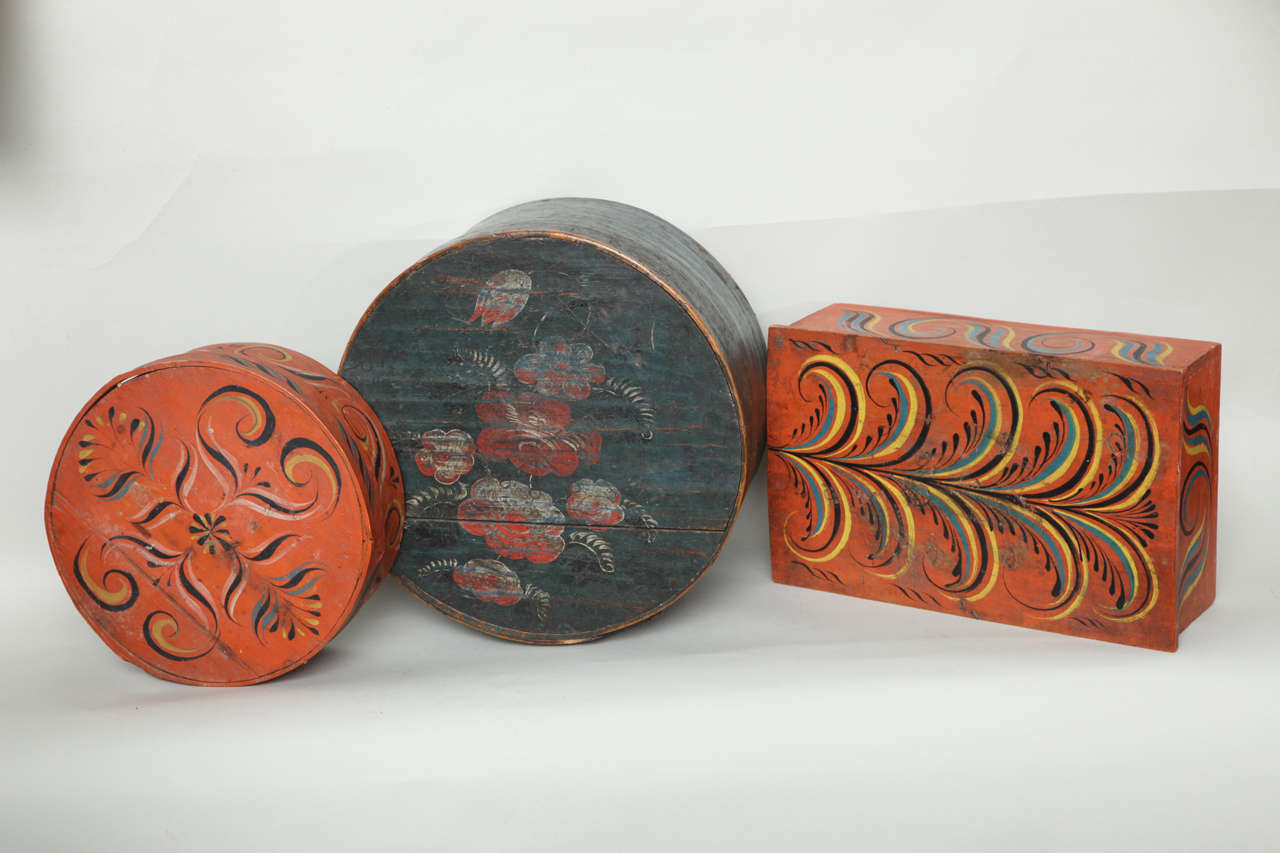 Pleasing assortment of three Norwegian folk decorated pantry boxes in original paint, two in salmon orange with stylized foliate designs, the third in deep dark robin's egg blue with floral design.  The two round boxes with bentwood and banded