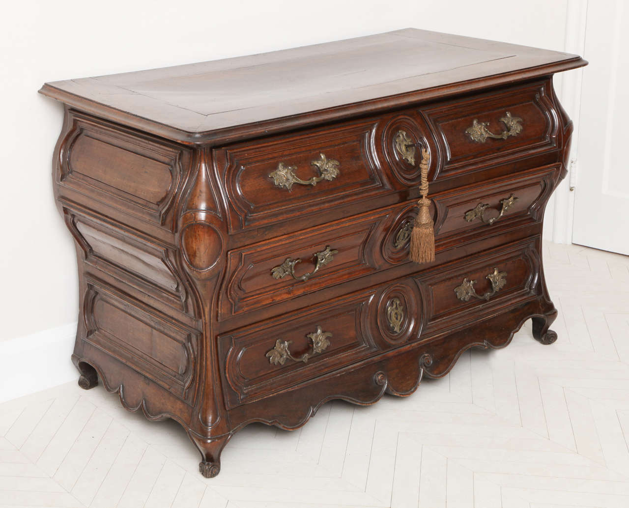 A Louis XV bombe-form walnut commode, the paneled rectangular top with moulded edge above three long carved drawers and a shaped apron flanked by moulded canted angles on shaped feet.