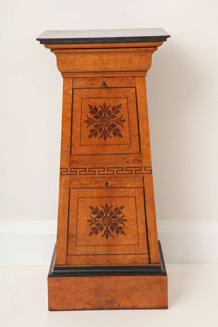 A Charles X bird's-eye maple tapered pedestal cabinet with amaranth inlay, a fossilized marble-top and two cabinet compartments, French, circa 1825.