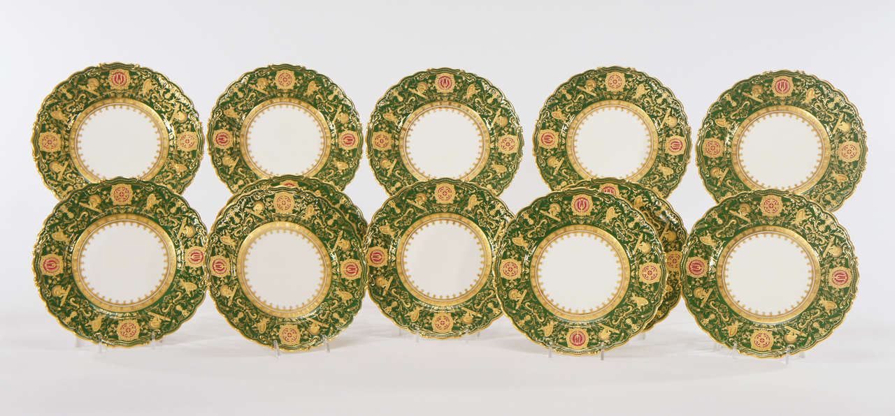 Set of 12 Coalport shaped rim green dessert plates with profuse raised paste gold depicting neoclassical motifs and musical Instruments. The forest green ground is embellished with four reserves in a ruby red with detailed neoclassical raised gold