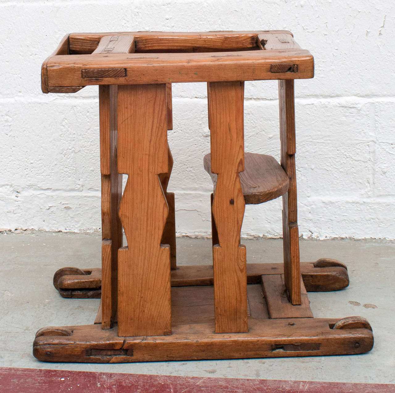 A delightful and fascinating infant's rolling low chair built of pitch pine and featuring superb through-tenon construction.  A small tray at the front can contain little amusements.  The wooden wheels have long since worn to ovals so it doesn't