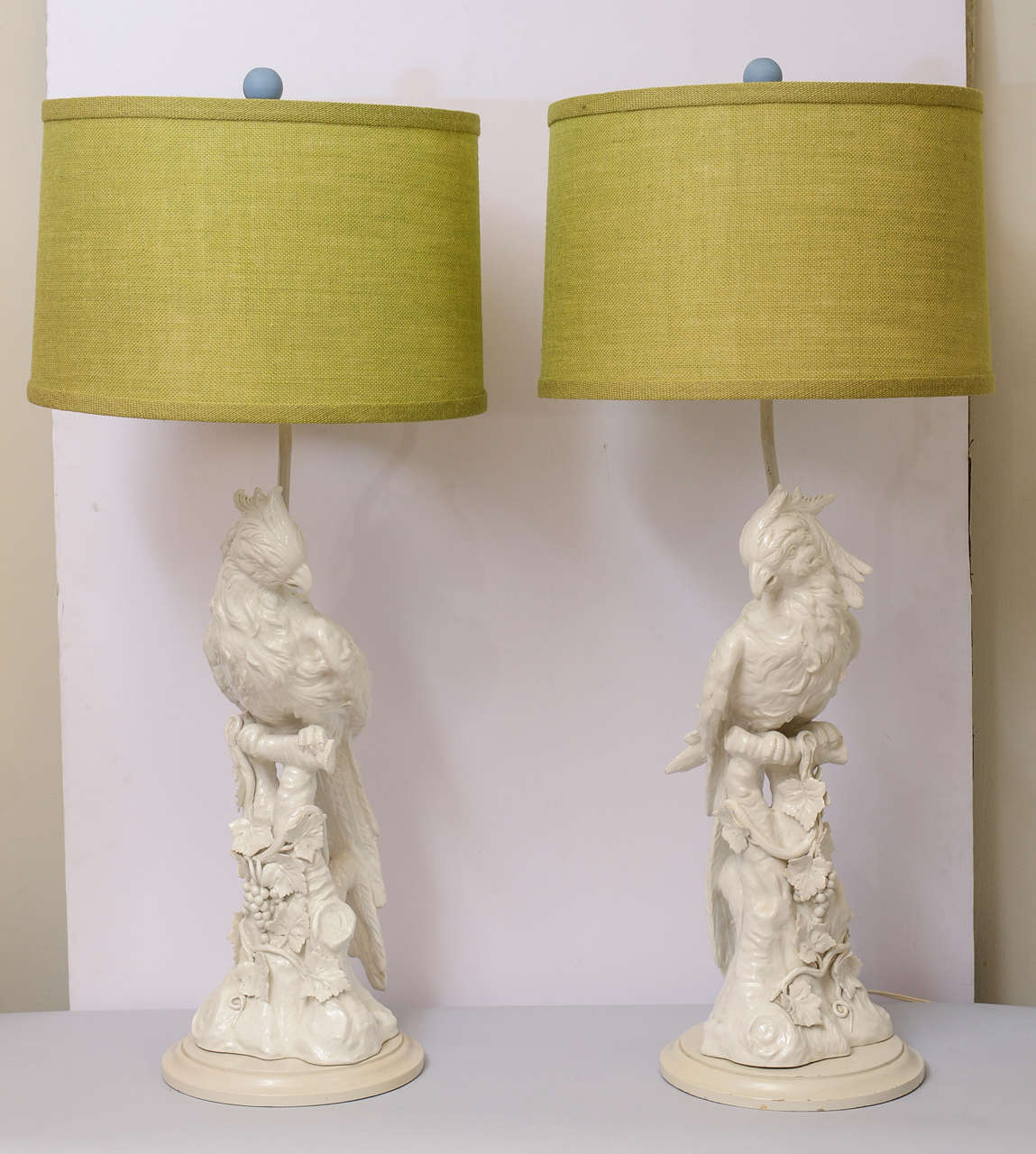 Pair of blanc de Chine lamps, each a beautifully detailed cockatiel resting on a branch with grape vines, on round base.  Shown with shades.