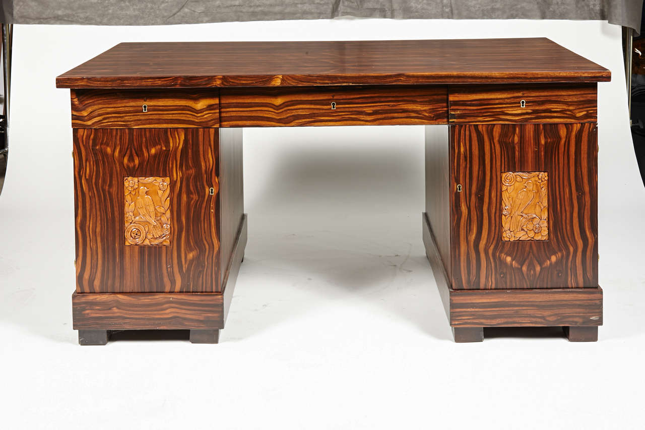 Very nice double-pedestal French rectilinear period art deco desk.
Finished in original gold-toned macassar, or the like, with inset carved sycamore Peruches panels and original brass piano hinges.

The desk is finished all-round in a beautifully
