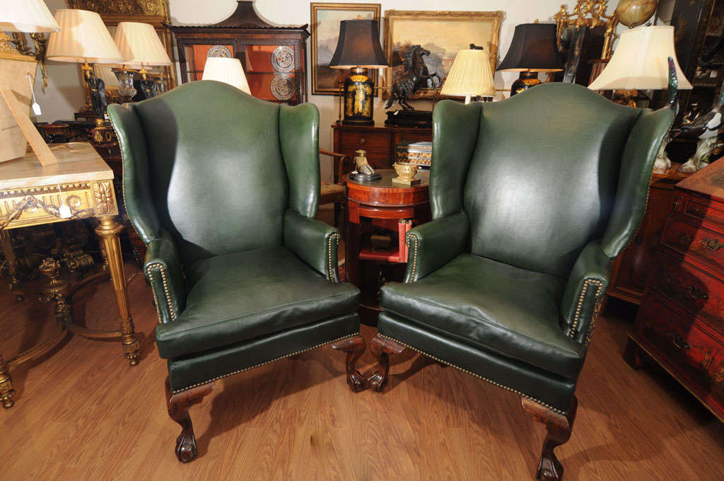 19th century English Chippendale Wing chairs. Hand carved Mahogany ball and claw feet. Covered in bottle Green leather and nail heads.
