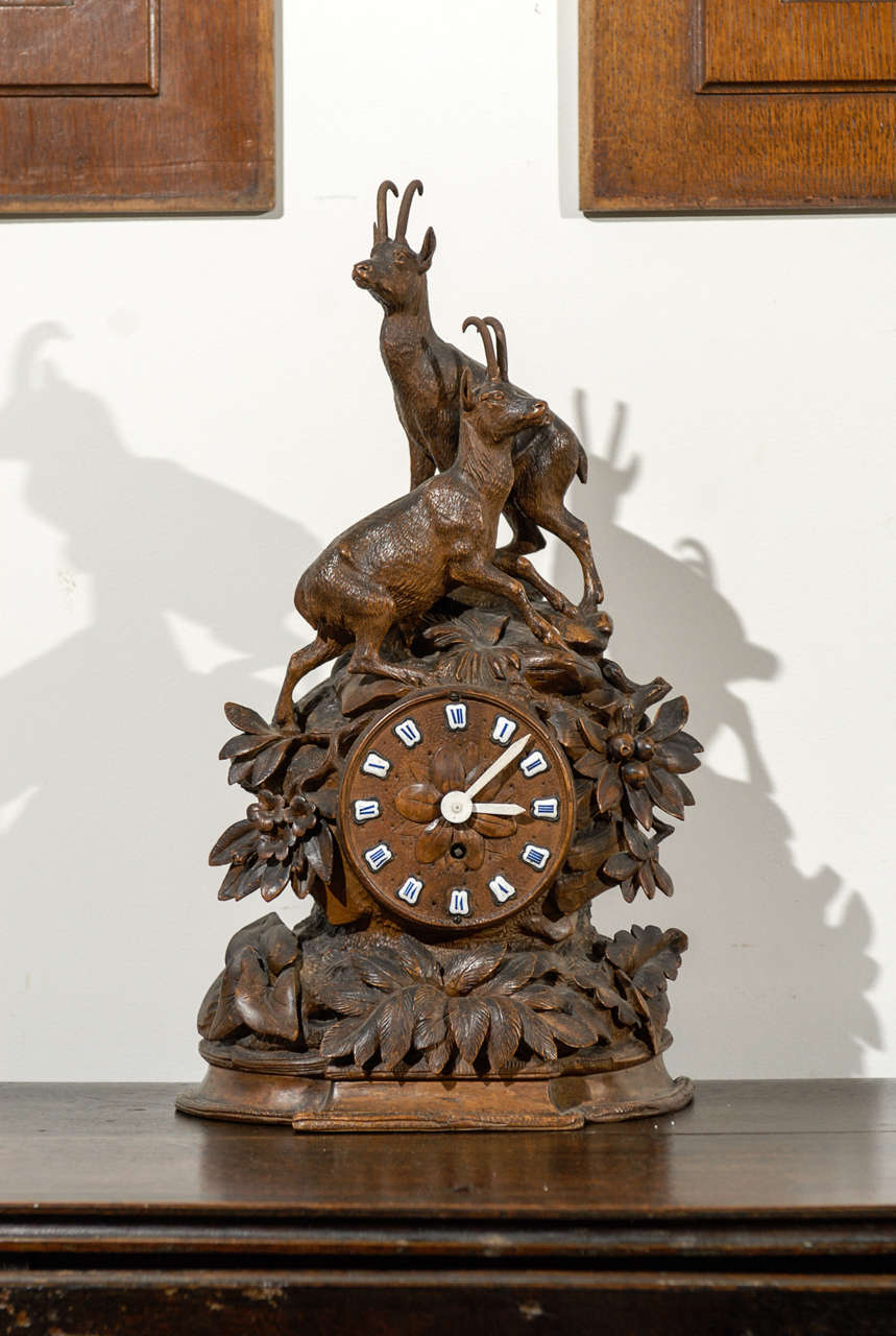 A German Black Forest carved wooden clock from the late 19th century with chamois figures and enameled Roman numbers. This Black Forest clock features a circular face, adorned with blue enameled Roman numbers, set within an exquisite carving. A