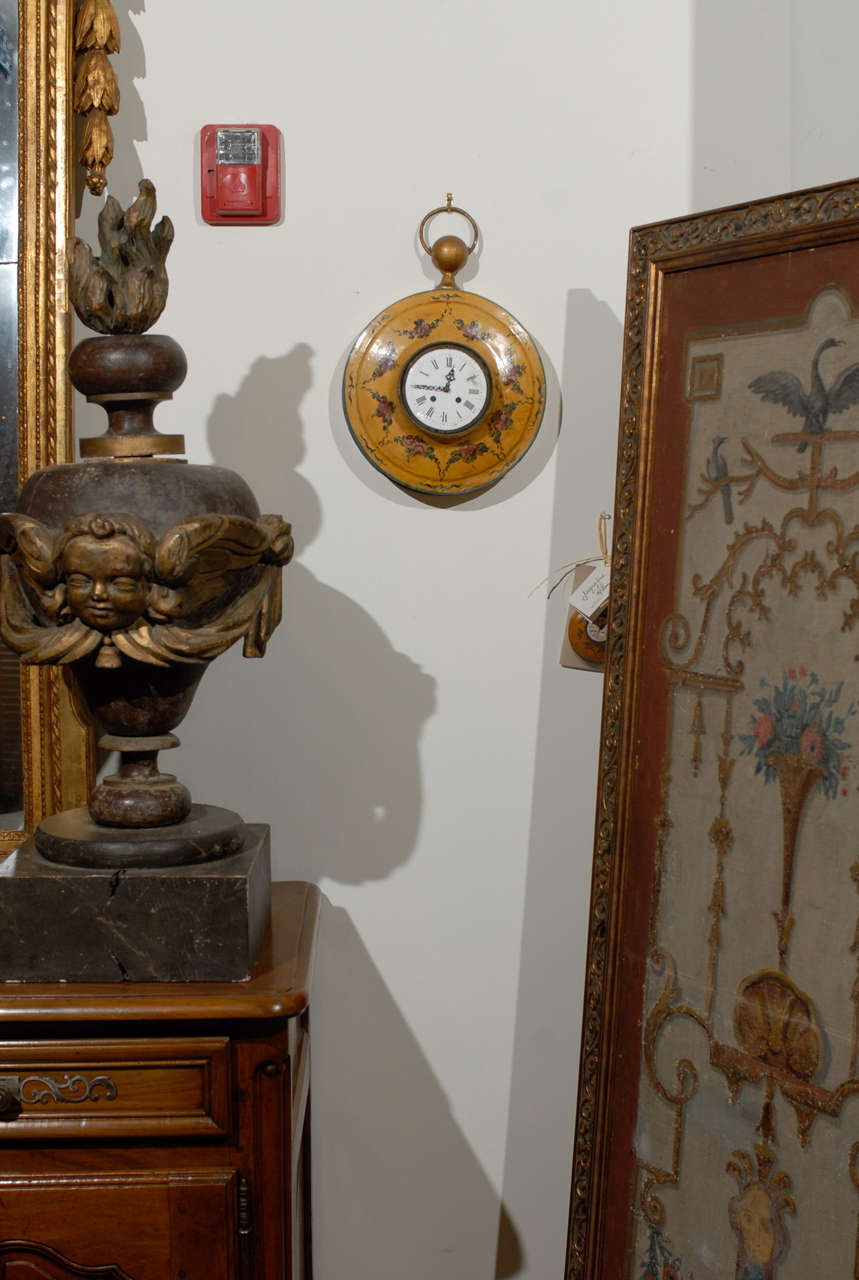 A French painted tôle pocket watch shaped wall-hanging clock with hand-painted floral décor from the early 19th century. This exquisite petite French wall clock is charmingly shaped like a pocket watch with a typical gilded circular bow at the top,
