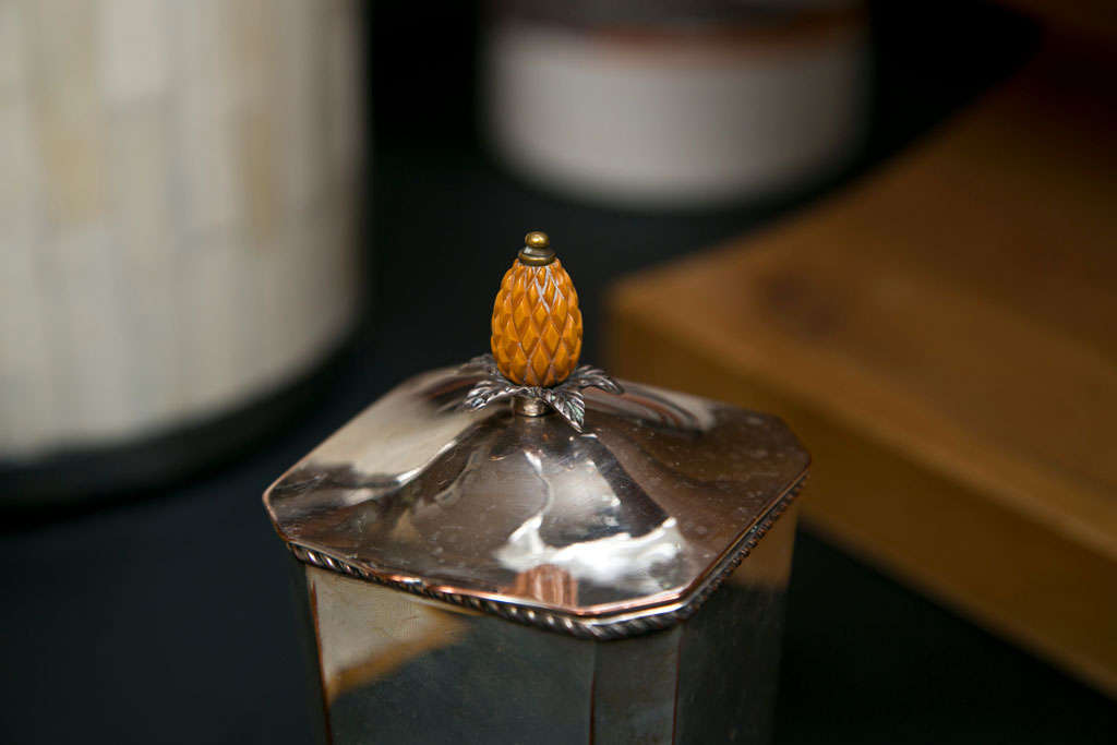 A stamped silver tea caddy with a delicate rope detail, topped with a carved ivory pineapple.