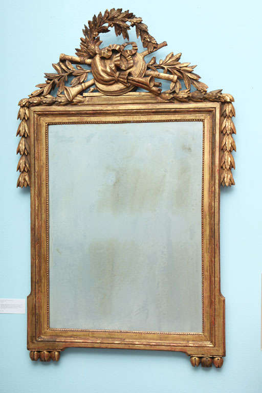 Neoclassical style frame of carved and giltwood with large, central antique mirror. The carved top features a musical trophy, laurel wreath, branches and bell flowers draped over the corners. Bottom corners feature carved bulbs.