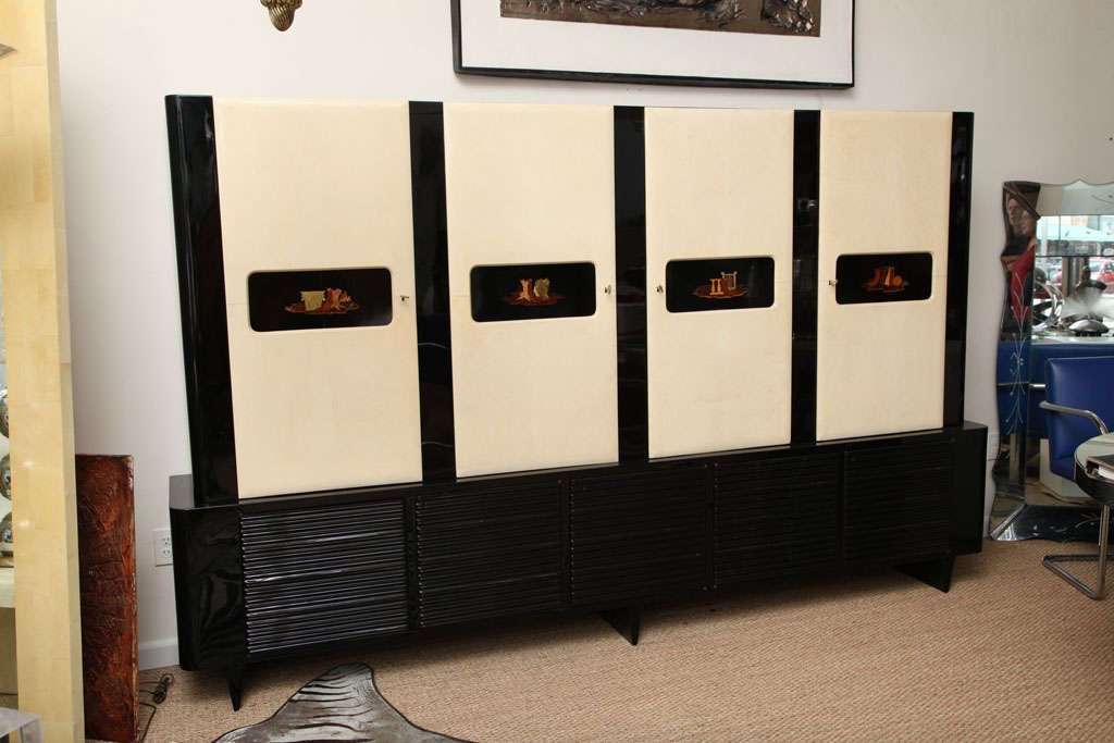 Art Deco tall, handsome and attention-grabbing trophy of 20th century Italian Cabinet, Buffet design and sophistication. 
Featuring four parchment covered doors with marquetry panels fronting an interior in black finish with shelves. All sitting on