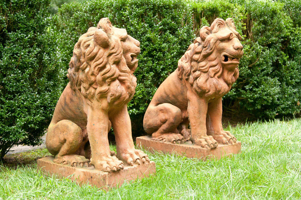 A pair of 17th-century style terra-cotta lions seated on their haunches, with animated expressions, their fully-maned heads turned in opposing directions.