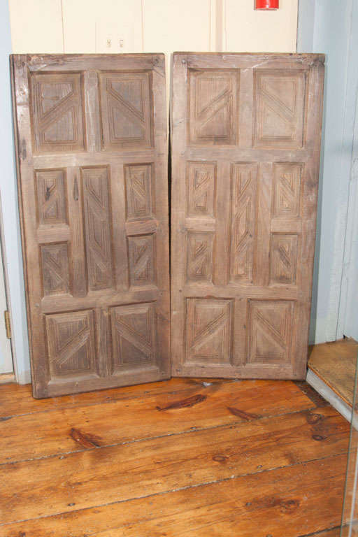 A pair of 17th Century Spanish Colonial paneled shutters with geometic design. These truly handsome shutters are hand carved and have a wonderful old dry surface with a warm patina. Mortise and pin construction, wire hangers are attached on the back