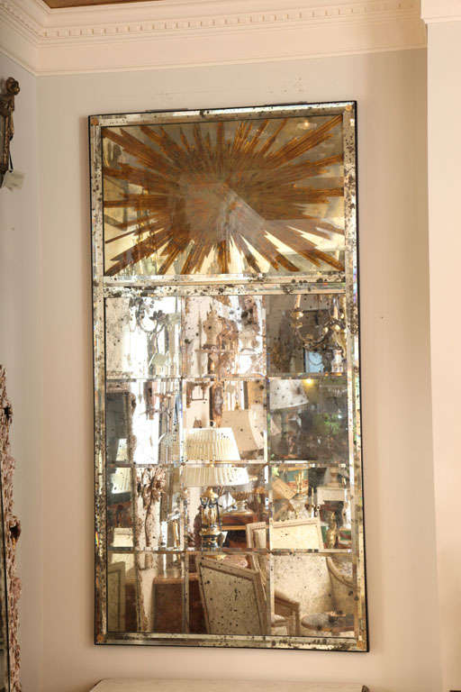 Mirror, of large scale, having twelve beveled panels of spotted mirror in mirrored frame, surmounted by reverse painted sunburst design.