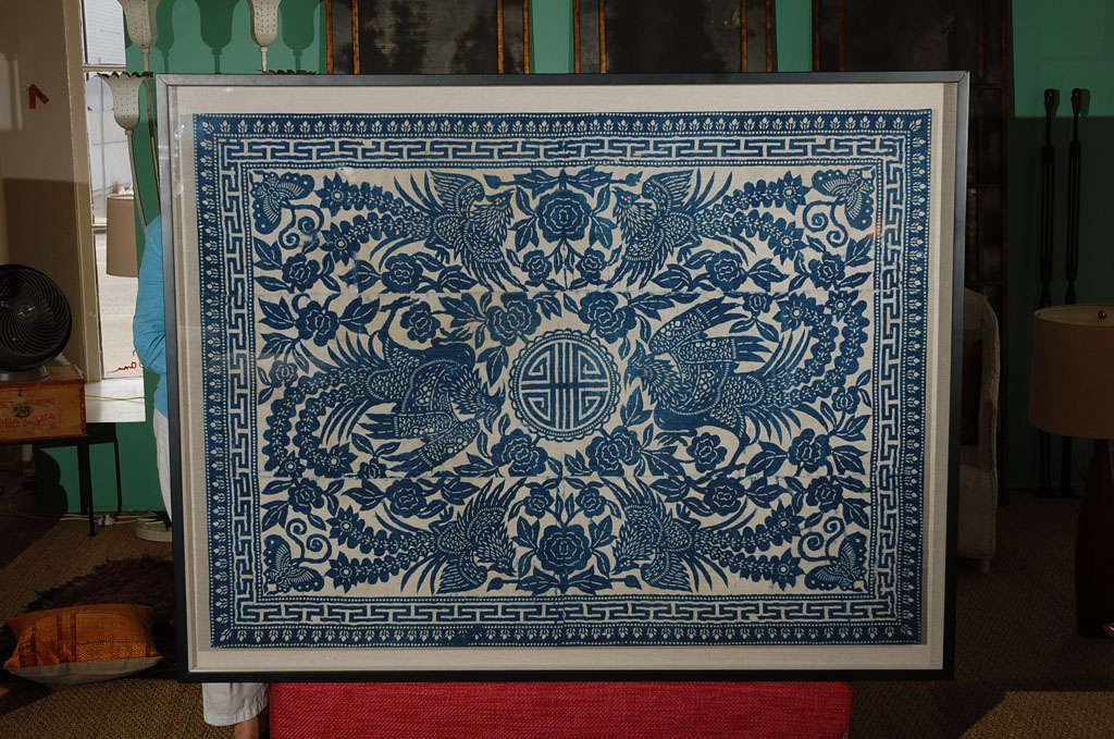 A framed Hmong block print textile depicting birds,flowers and butterflies. It has been mounted on a stretcher with a black lacquer frame and a linen background.