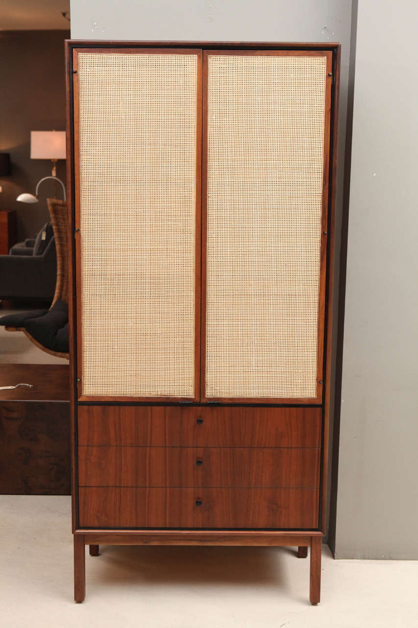 Tall walnut and cane cabinet with drawers at bottom and leather door pulls.