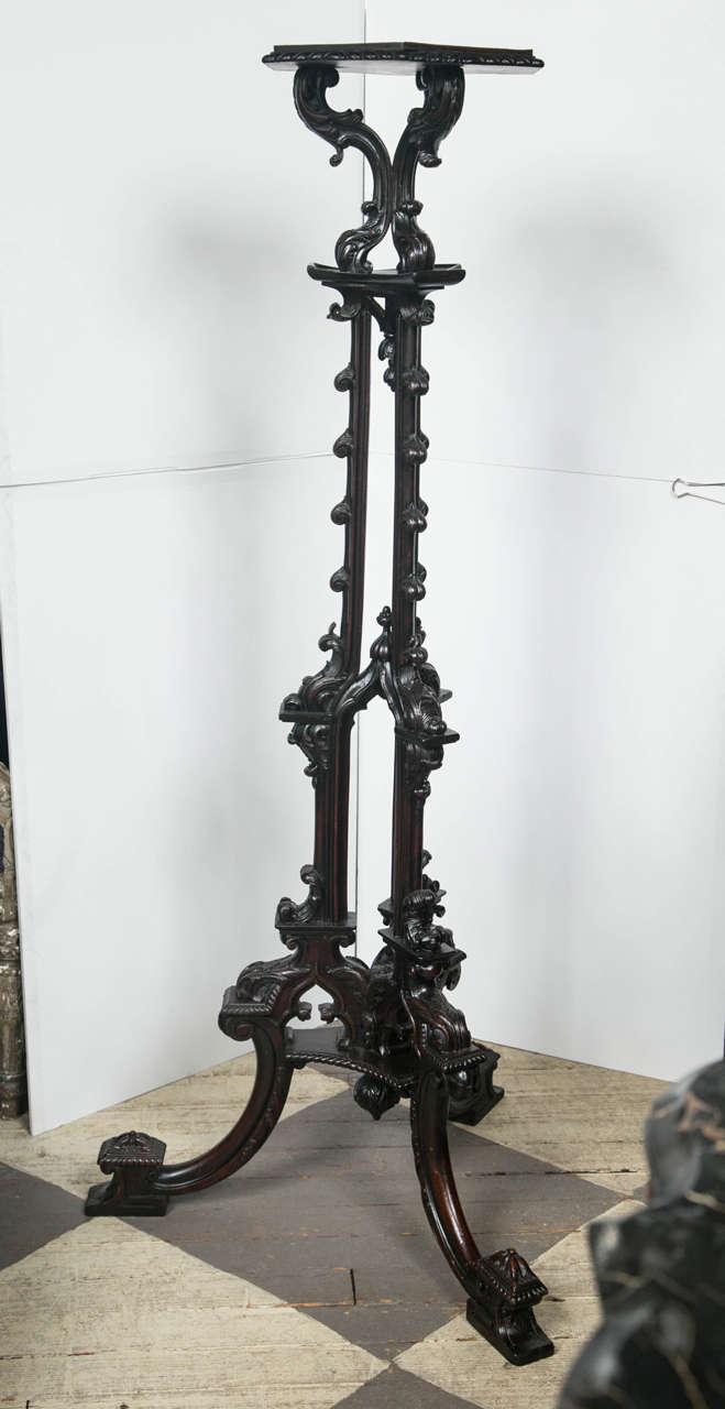 This  highly decorative stand is made of dark mahogany. The top is six sided with  gardrooned edge. A triplex of supports and uprights, all carved in the gothic revival manner, lead to the splaying  three legged base. The top has an 11 inch