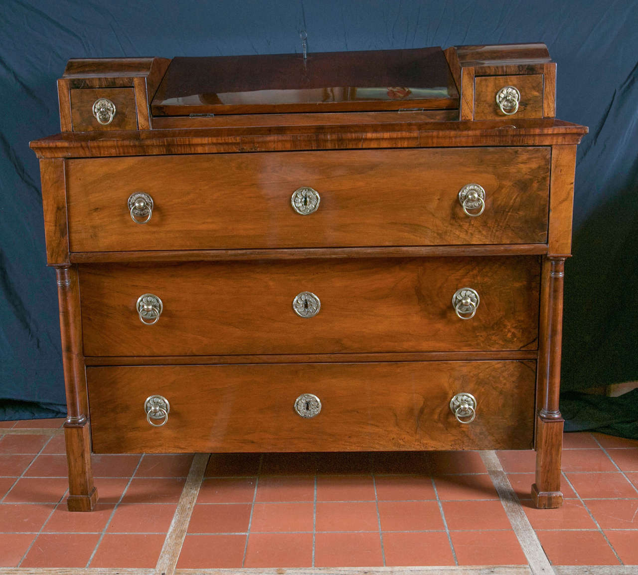 The handsome lines of this chest augment its wonderful proportions with drawers flanking the center drop down writing surface. Deeper than the two below, the top drawer is supported by finely turned columns that terminate in square plinths. Brass