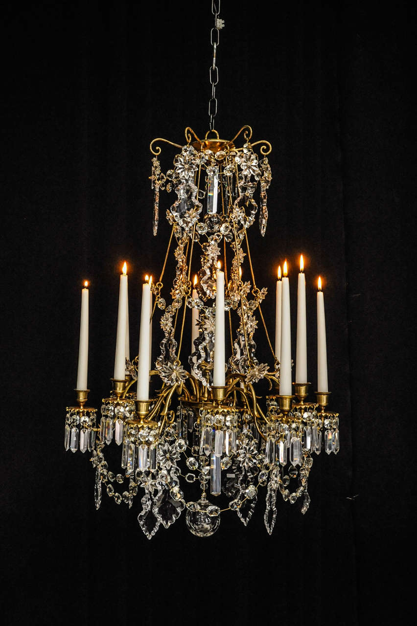 A gilded bronze and glass 12 arms chandelier attributed to Baccarat. The central receiver plate, receiving the 12 arms on which hang moulded glass pendants, chains of octogonal drops,and on each of the drip-pans nine more drops with pendants. On six