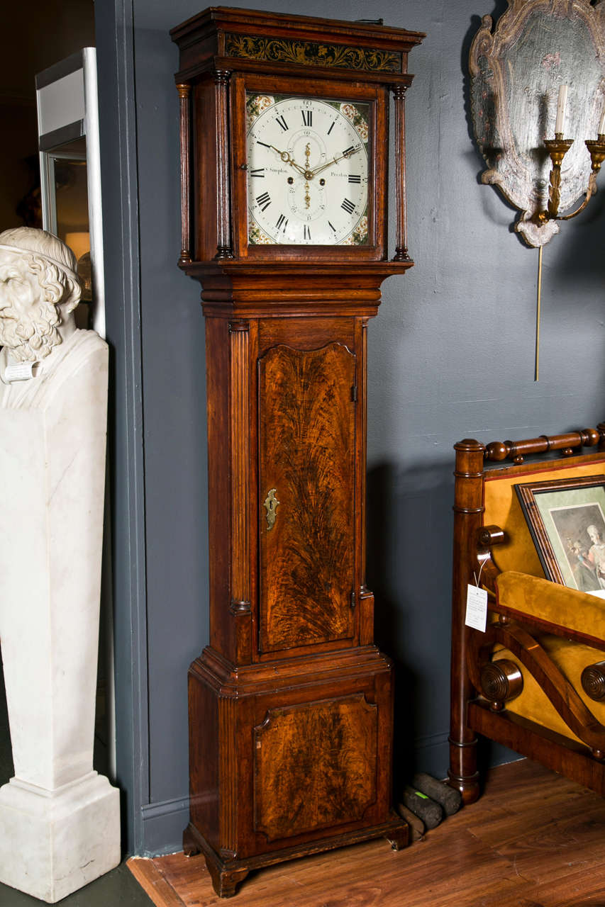 A good and charming English late 18th century grandfather clock with simulated verre églomisé panel above the painted dial, signed S. Simpson, Preston. The flame mahogany paneled door and base on oak case with a square 8-day movement in neoclassical